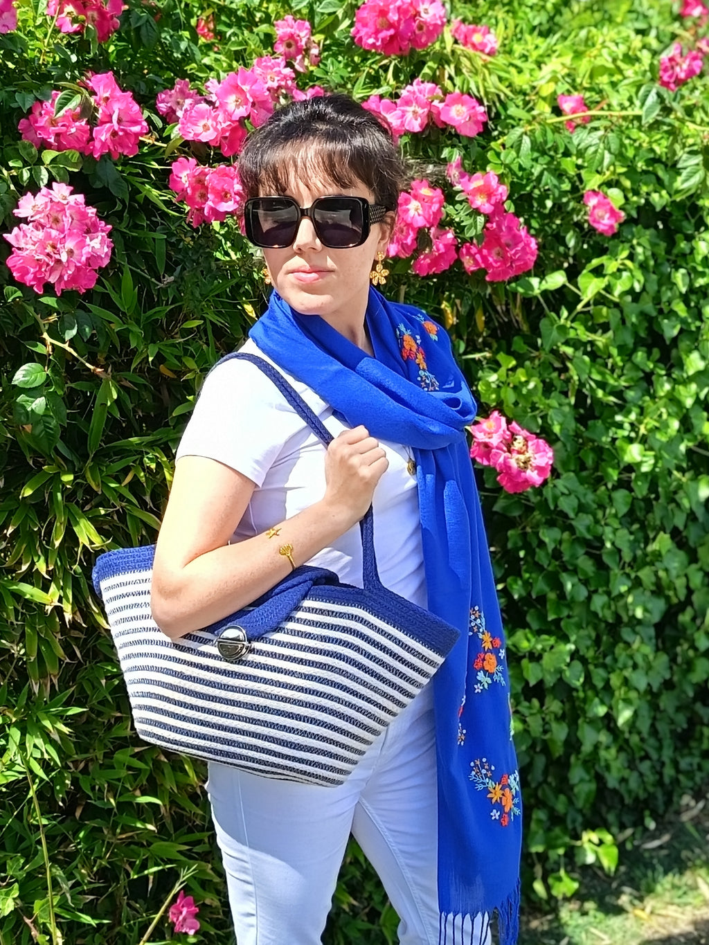 Une femme dans un jardin qui porte l’écharpe brodée Samar bleue et le sac à main Alexandrie Niléa