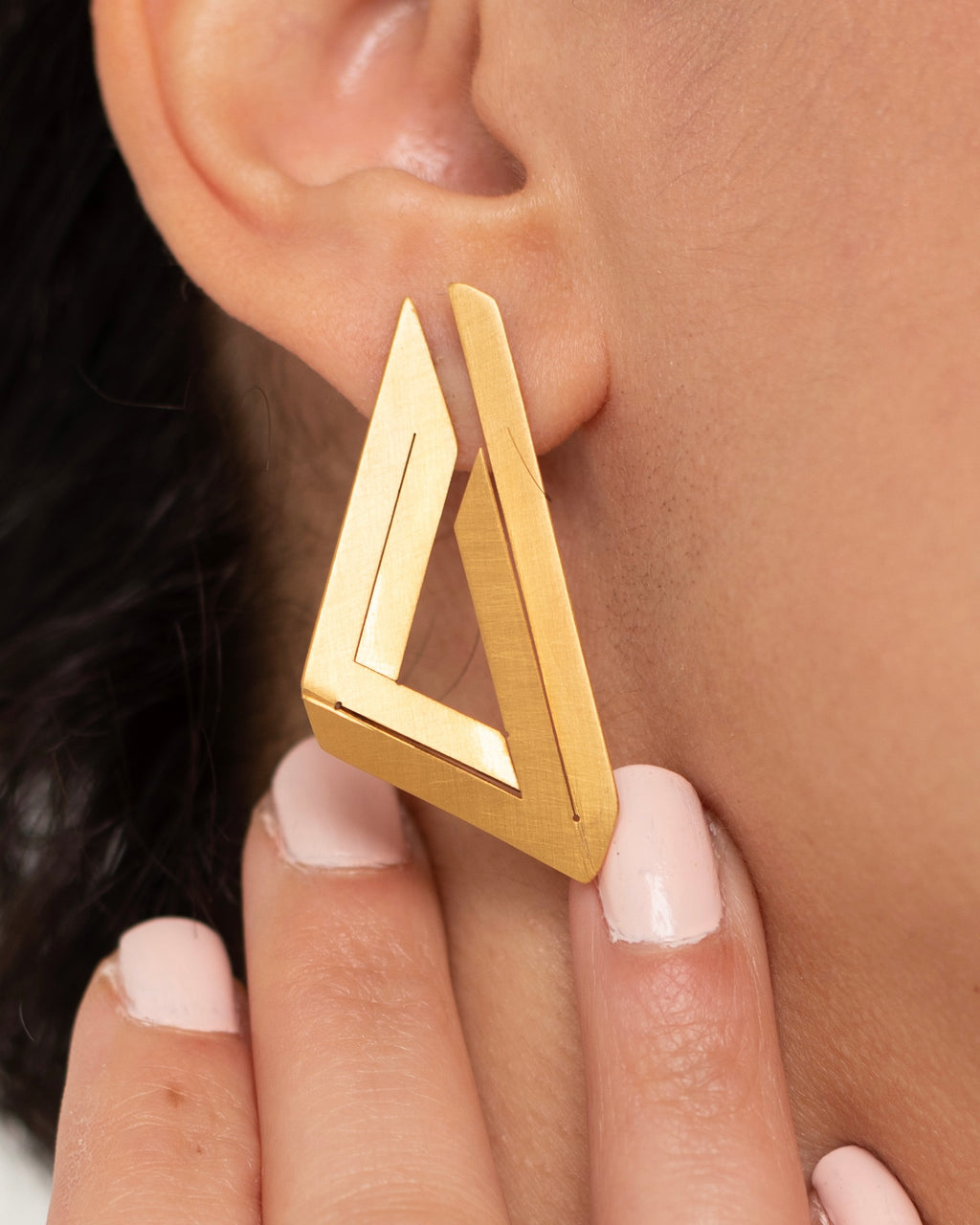 Boucles d’oreilles Le Triangle Impossible portées, bijou en laiton doré à l'or fin au design graphique.