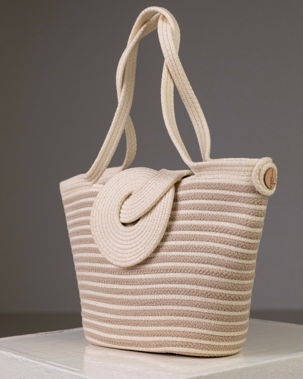 Sac cabas Dahab de Maison Niléa à rayures horizontales blanc et beige, confectionné en corde de coton égyptien tressée avec un rabat texturé en relief et de longues anses pour un porté épaule, présenté sur un fond gris.