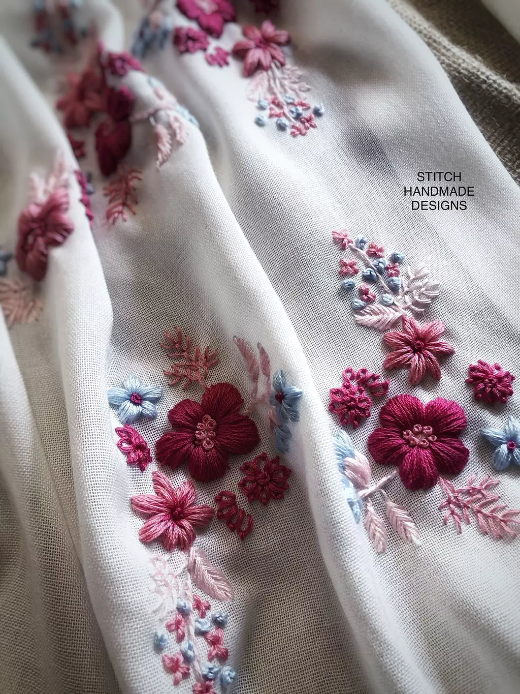 Détails de la broderie rose, Fuchsia et bleu ciel faite main sur l'écharpe Dalia écrue Niléa. 