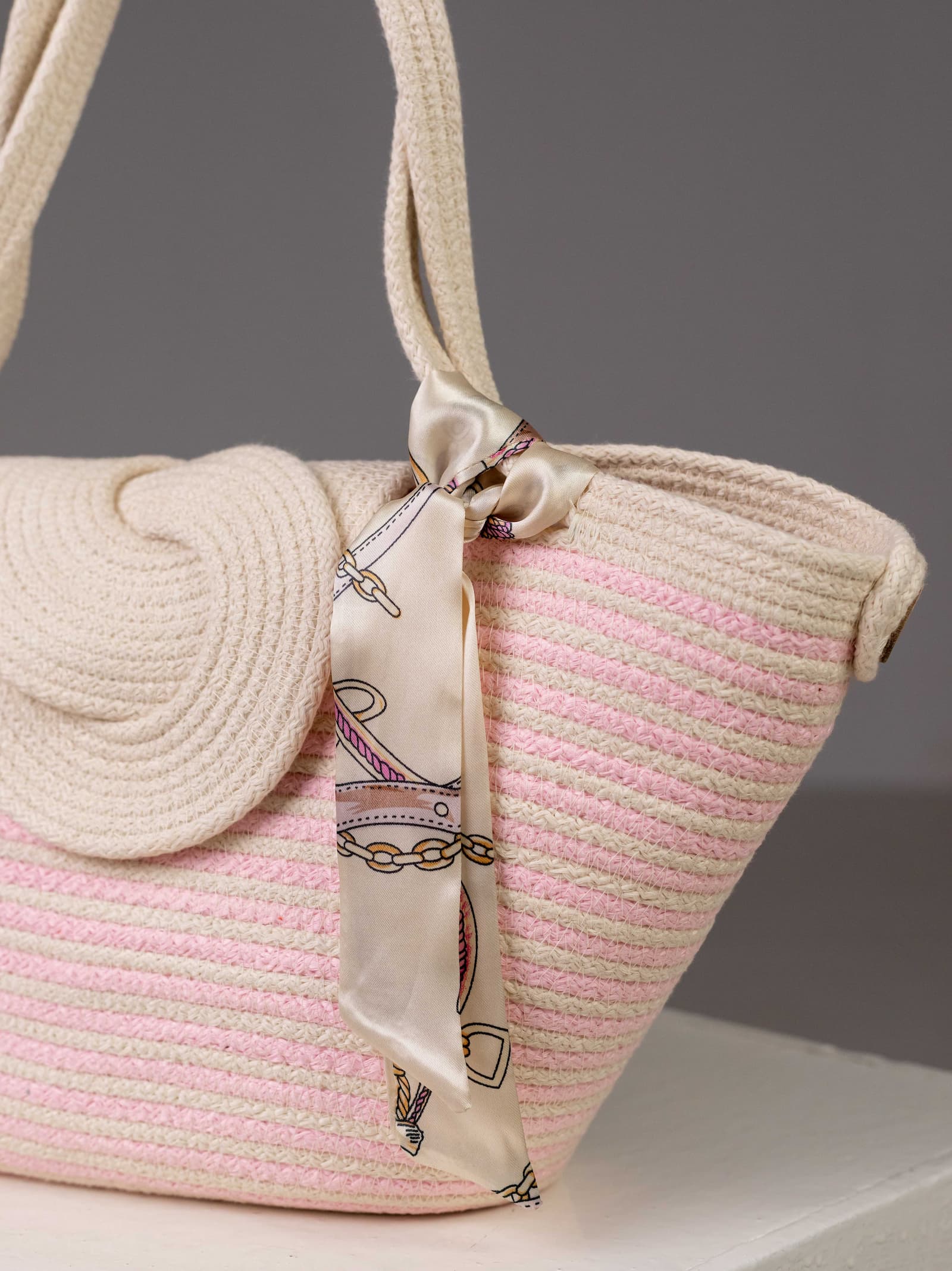 Gros plan sur la poignée du sac Héliopolis, mettant en évidence le foulard en satin aux motifs de chaînes dorées et de boucles, délicatement noué sur l'anse en corde tressée.