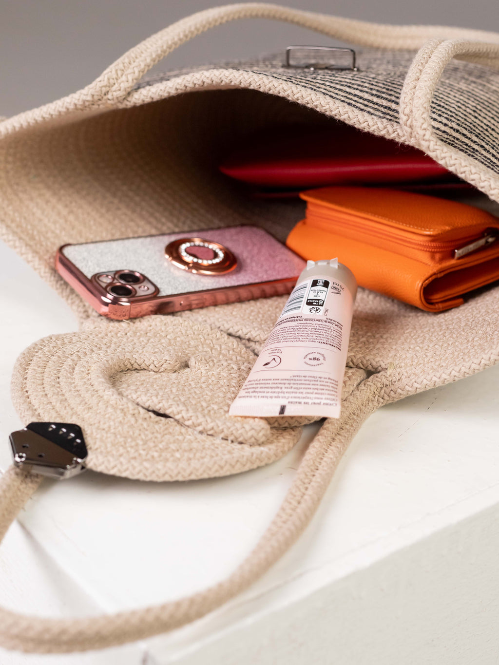 Vue de l'intérieur du sac cabas Sahara ouvert, montrant sa belle contenance avec un téléphone, un portefeuille orange et une crème pour les mains.