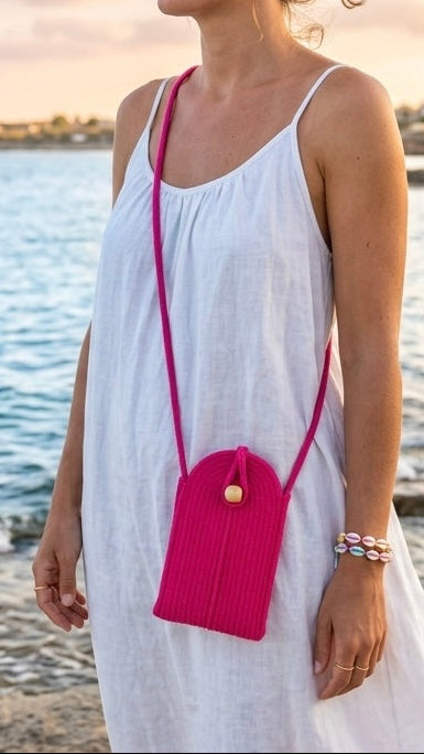 Pochette mobile fuchsia portés sur une robe blanche au bord de la mer.