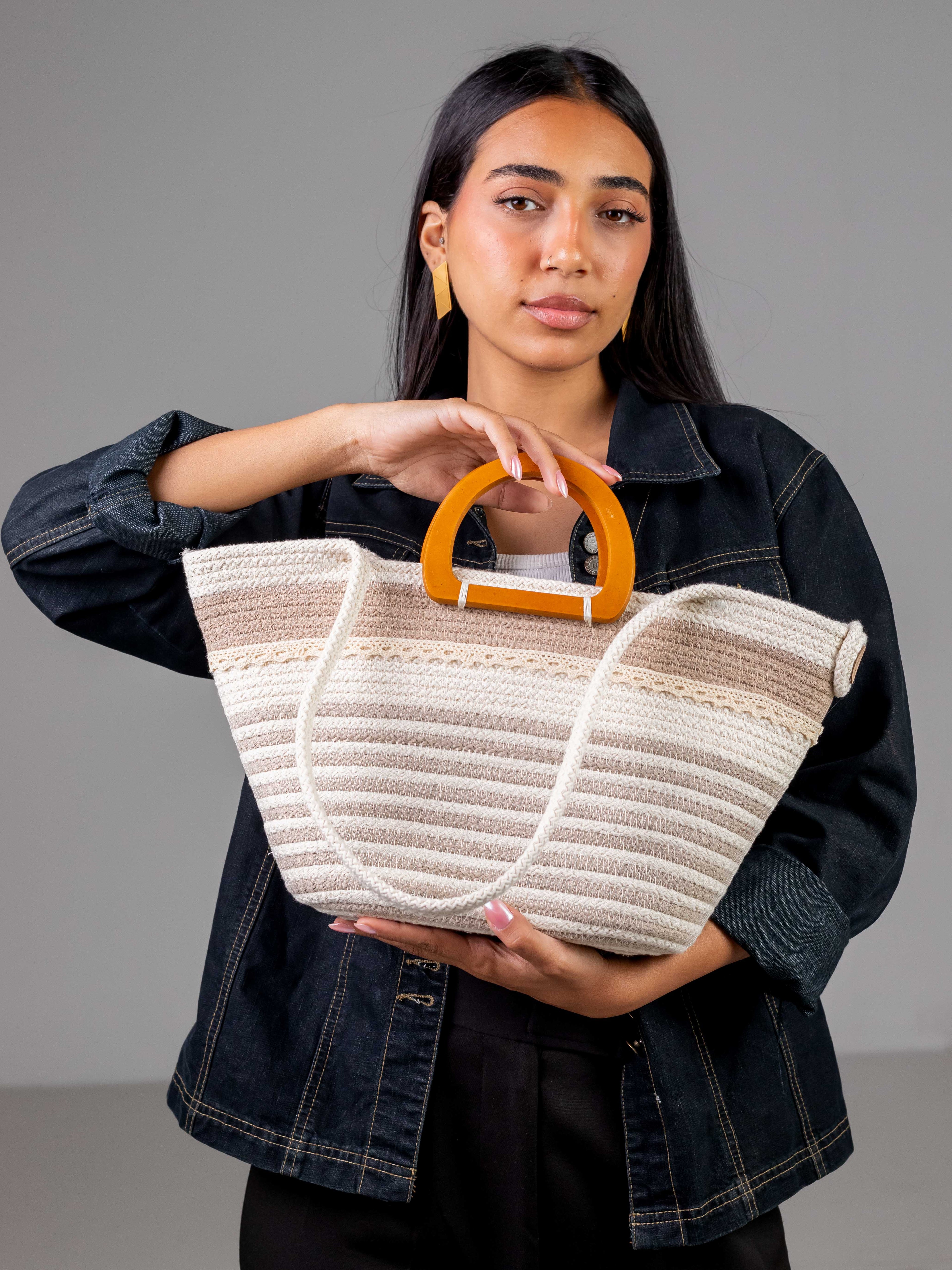 Mannequin portant à la main le sac cabas Farafra bicolore blanc et beige, associant des anses en bois et une tenue en jean moderne.