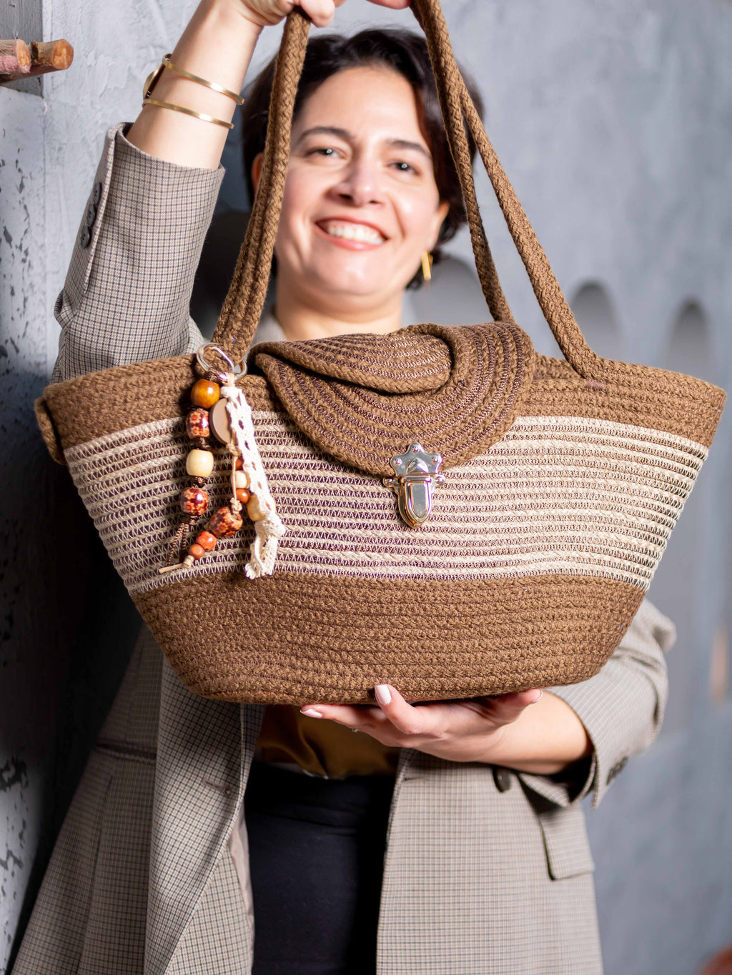 Mannequin souriant portant le sac cabas Gizeh de Maison Niléa, mettant en valeur son design bicolore marron et taupe, ses anses en corde tressée et son charm amovible attaché à l'anse.