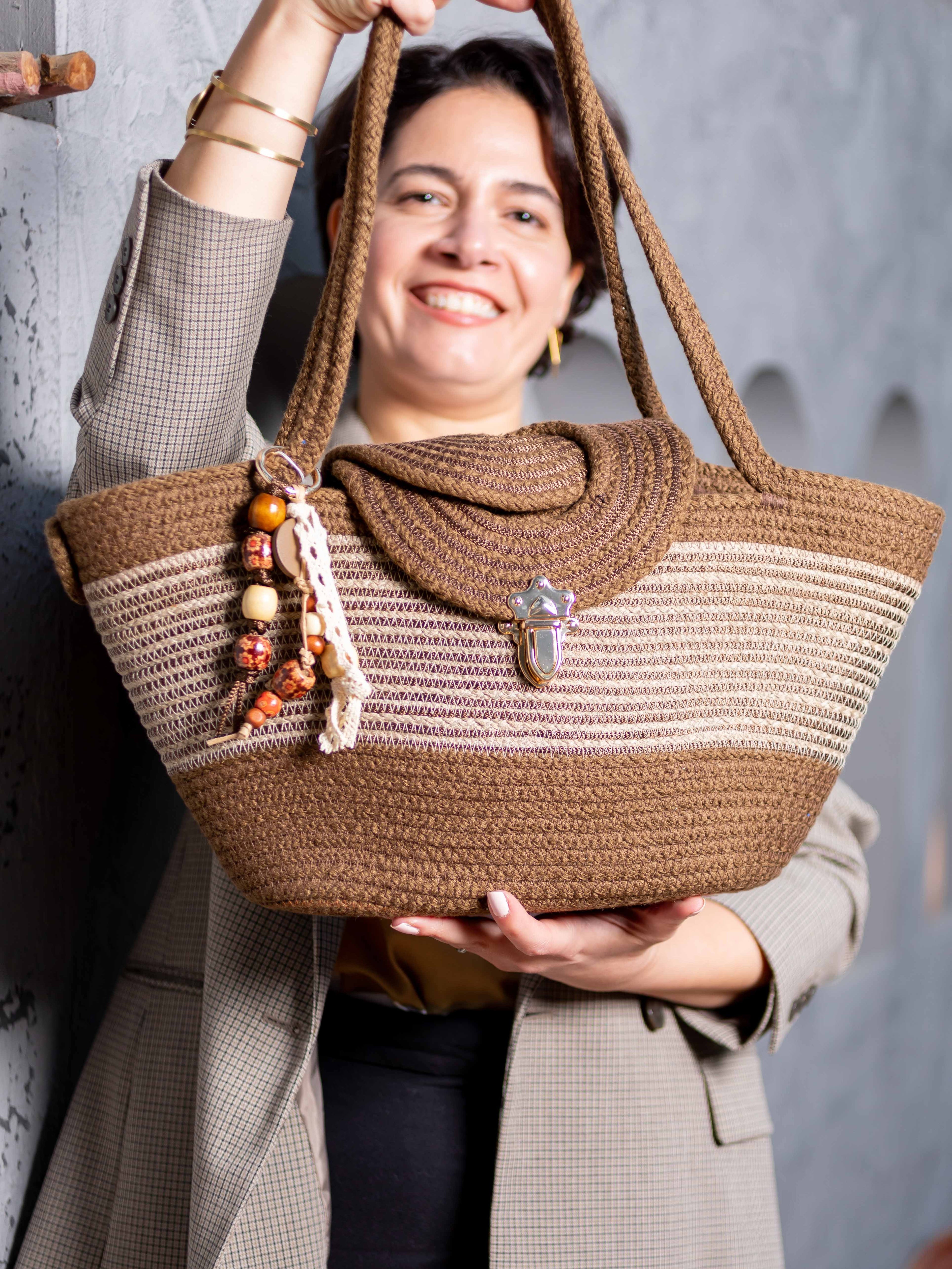 Mannequin souriant portant le sac cabas Gizeh de Maison Niléa, mettant en valeur son design bicolore marron et taupe, ses anses en corde tressée et son charm amovible attaché à l'anse.