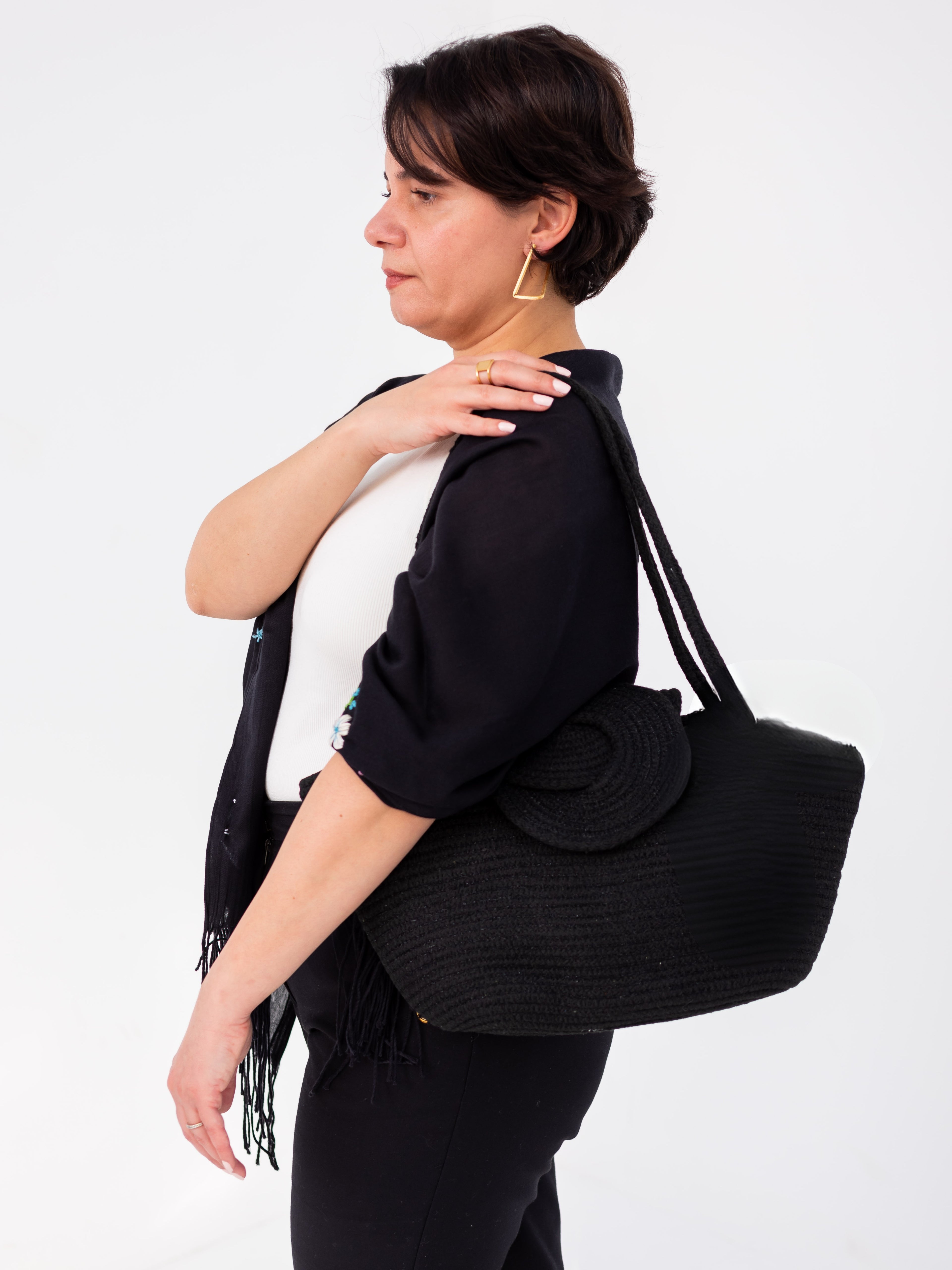 Femme portant le sac cabas Nout noir pailleté à l'épaule, montrant sa taille et son porté, sur fond blanc. Elle porte l'écharpe Leila noir à broderies fait main signé Niléa également.