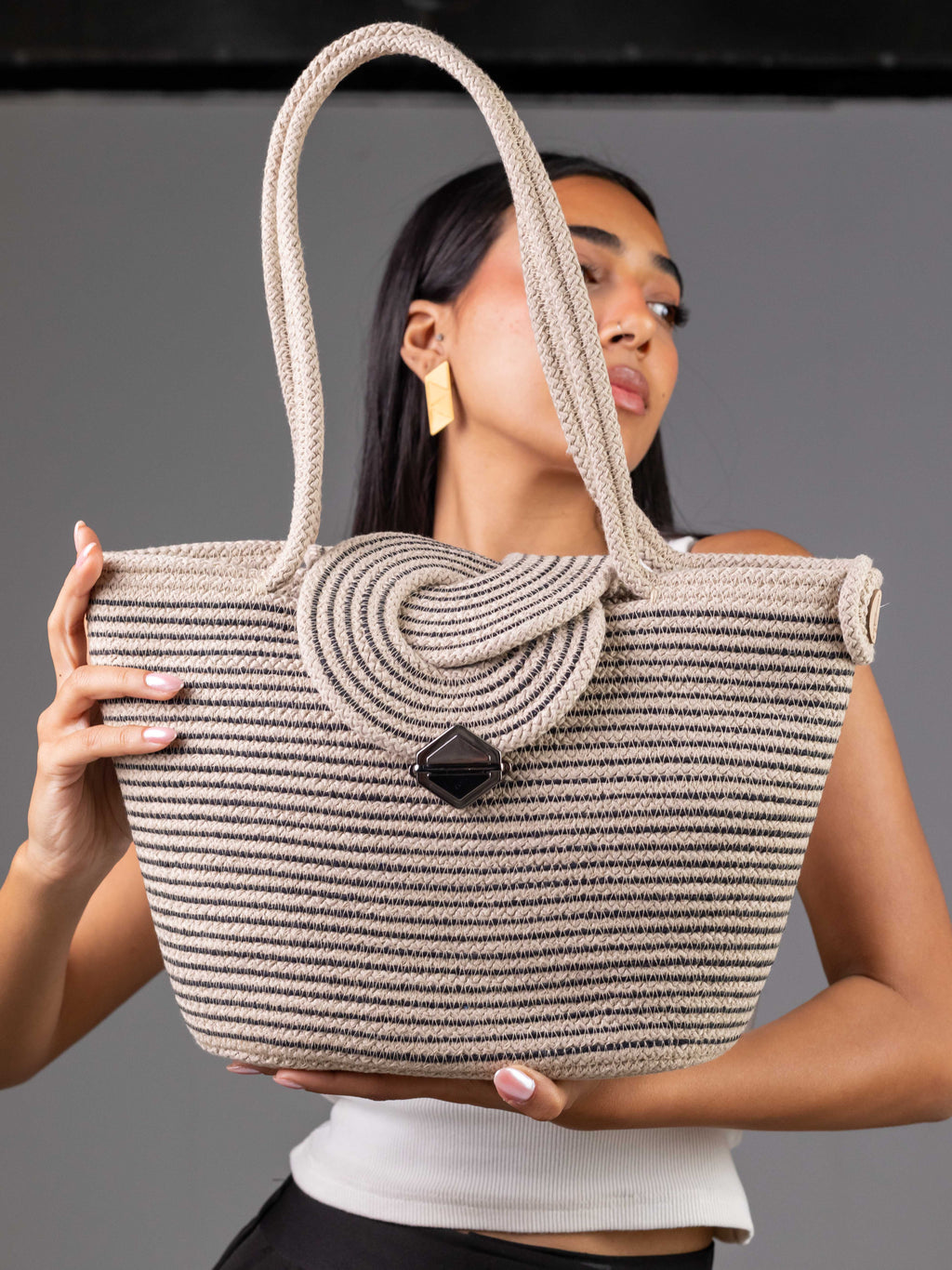 Sac cabas Sahara beige à rayures noires de Maison Niléa porté à la main par un mannequin, mettant en valeur son fermoir géométrique noir et ses longues anses.