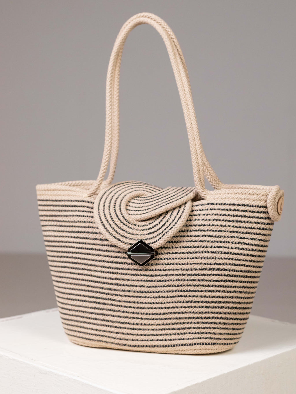 Sac cabas Sahara bicolore beige et noir en corde de coton tressée, posé en studio avec son rabat en relief et son fermoir design.
