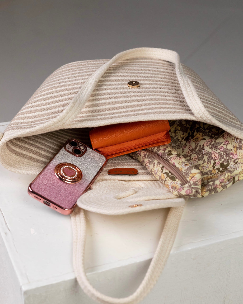 Vue de l'intérieur ouvert du sac cabas Dahab de Maison Niléa, révélant sa grande capacité de rangement avec un smartphone, une trousse et un portefeuille, ainsi que le bouton de fermeture magnétique discret.